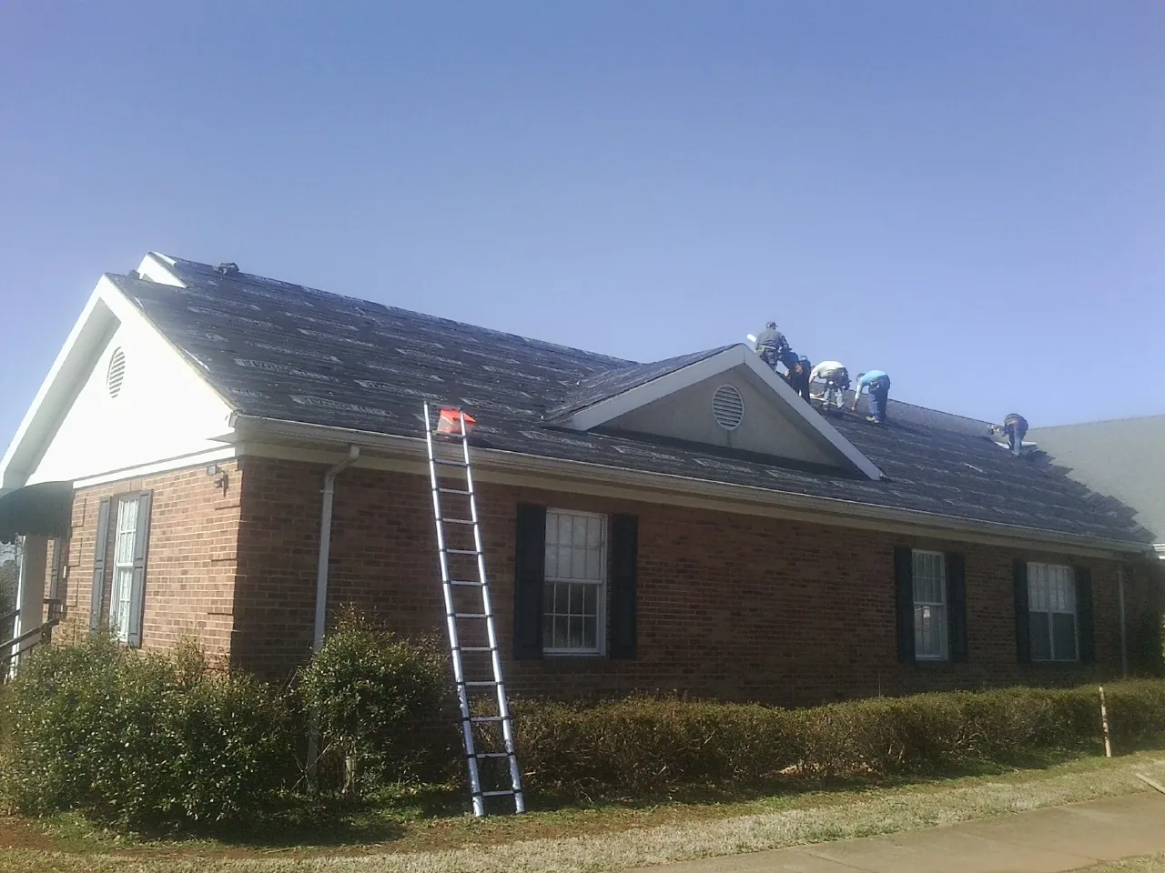 Crew tearing shingles off a brick ranch roof with a ladder set — Metal Roof Repair work by our crew in Represa