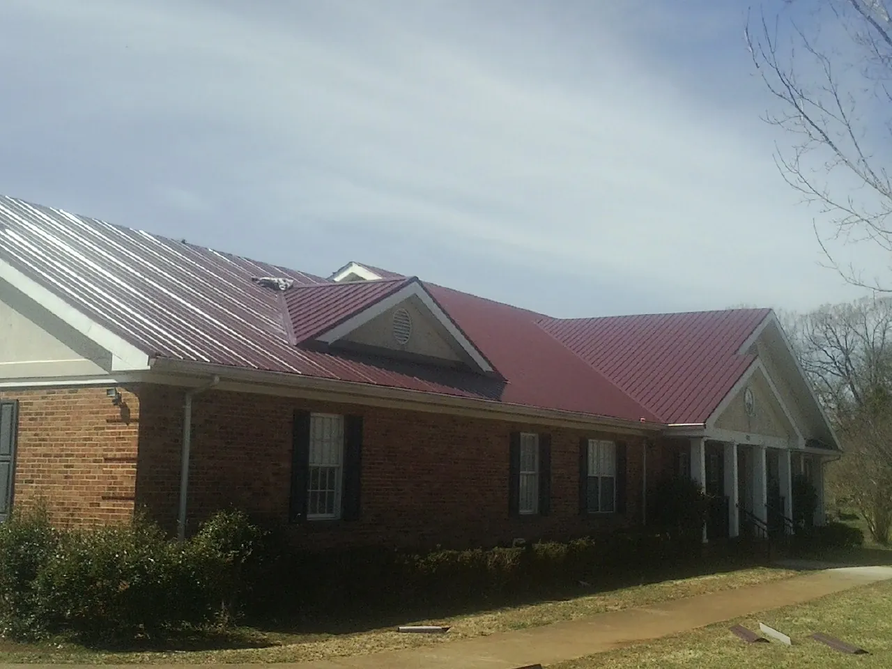 Red metal roof with gabled entries on a long brick building, from a Hail Damage Roof Repair job in Represa