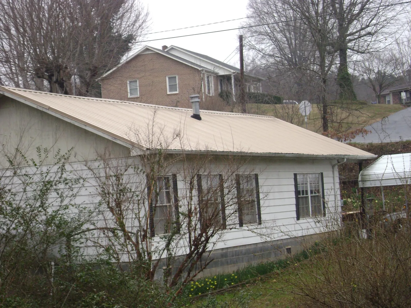 Tan metal roof on a white sided house set into a hillside — Commercial Roofing by Roofing Brothers in Represa